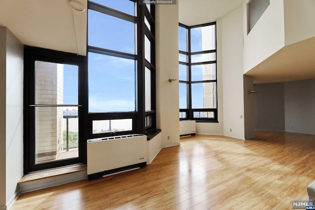 unfurnished living room featuring radiator, a towering ceiling, light wood-type flooring, and a wealth of natural light