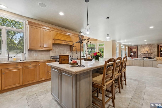 kitchen with pendant lighting, custom exhaust hood, a center island, a kitchen breakfast bar, and a brick fireplace