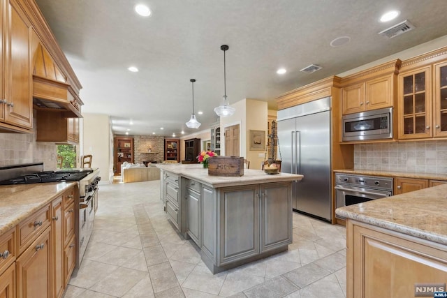 kitchen with built in appliances, a kitchen island, light stone countertops, and hanging light fixtures