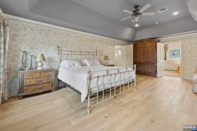 bedroom featuring light wood-type flooring, a tray ceiling, baseboard heating, and ceiling fan