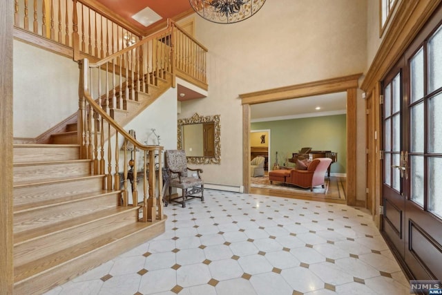 foyer featuring french doors, a baseboard heating unit, crown molding, an inviting chandelier, and a high ceiling