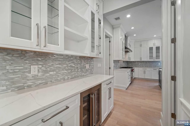 kitchen featuring high end range, backsplash, light hardwood / wood-style flooring, light stone counters, and white cabinetry