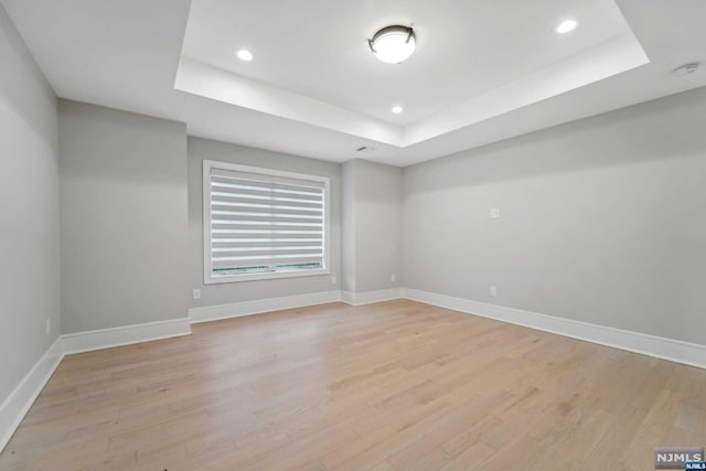 spare room featuring a tray ceiling and light hardwood / wood-style floors