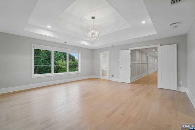 unfurnished room with a chandelier, light hardwood / wood-style floors, and a tray ceiling