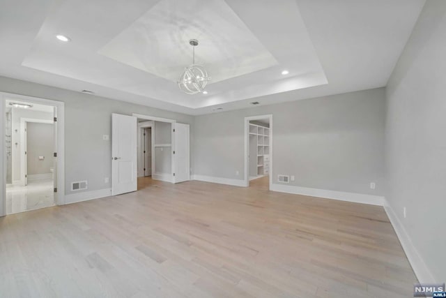 unfurnished bedroom with a raised ceiling, a walk in closet, light wood-type flooring, and a closet