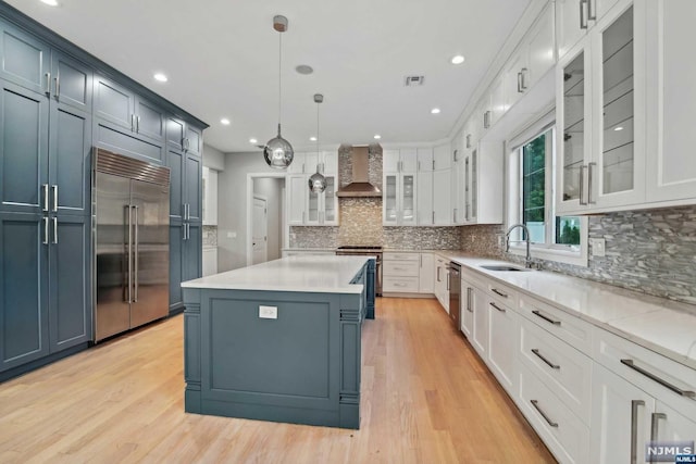 kitchen featuring hanging light fixtures, stainless steel appliances, wall chimney range hood, and light hardwood / wood-style flooring