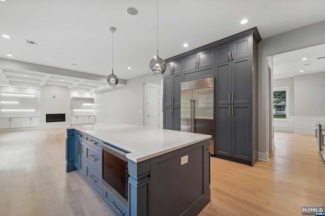 kitchen with coffered ceiling, light stone counters, light hardwood / wood-style flooring, built in appliances, and decorative light fixtures