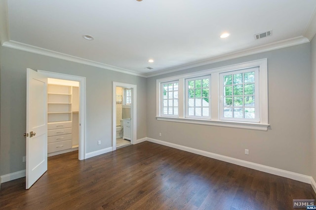 unfurnished bedroom with crown molding, connected bathroom, a walk in closet, a closet, and dark hardwood / wood-style flooring