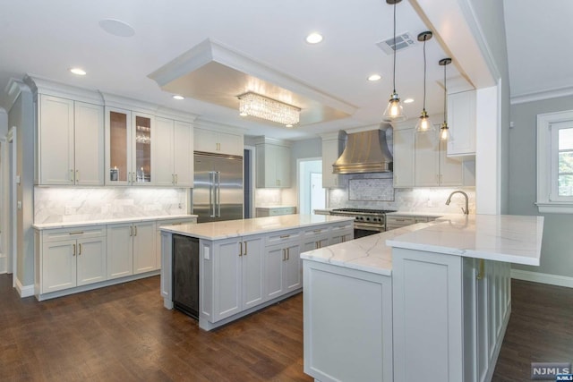 kitchen with white cabinetry, wall chimney exhaust hood, high quality appliances, and hanging light fixtures