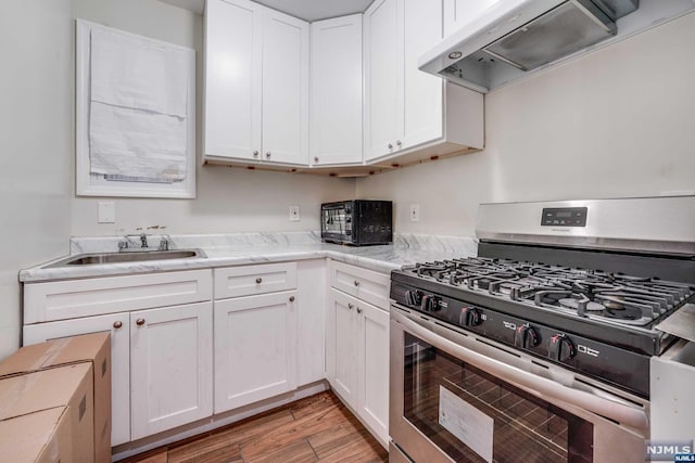 kitchen with exhaust hood, white cabinets, sink, stainless steel gas range, and light wood-type flooring