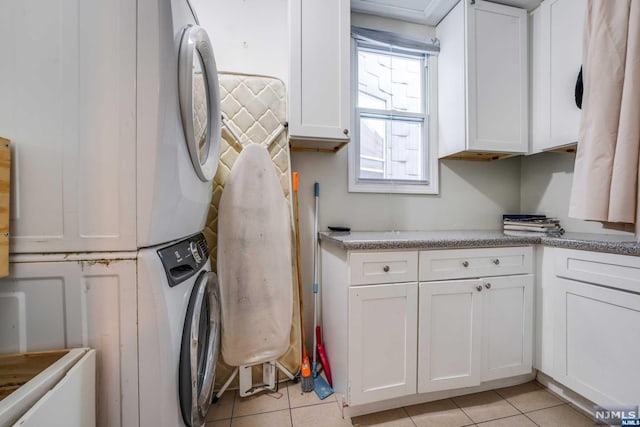 laundry area featuring cabinets, light tile patterned floors, and stacked washing maching and dryer