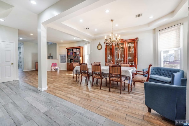 dining area with a chandelier, light hardwood / wood-style floors, and a tray ceiling