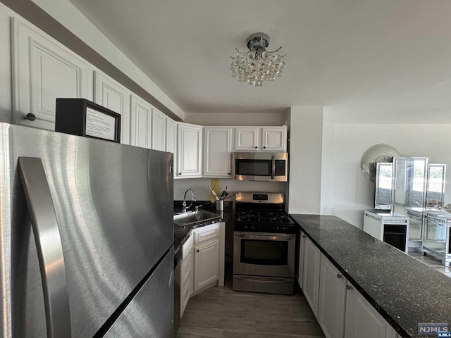 kitchen with appliances with stainless steel finishes, dark wood-type flooring, sink, an inviting chandelier, and white cabinets