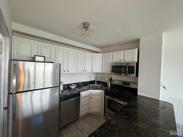 kitchen with white cabinets, sink, dark stone countertops, light wood-type flooring, and appliances with stainless steel finishes