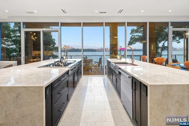 kitchen with a spacious island, light stone countertops, a water view, and a healthy amount of sunlight