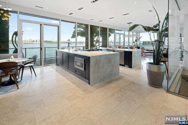 kitchen with floor to ceiling windows, sink, a center island with sink, a water view, and appliances with stainless steel finishes