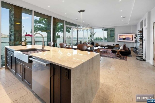 kitchen featuring light stone counters, stainless steel dishwasher, an island with sink, pendant lighting, and a water view