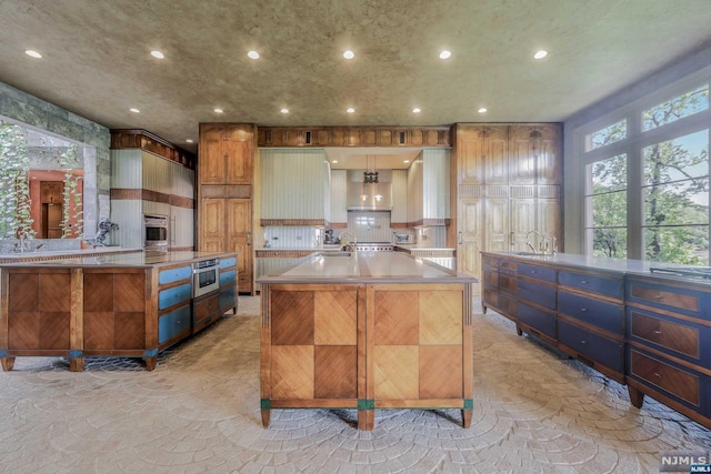 kitchen featuring sink, stainless steel appliances, backsplash, a large island with sink, and kitchen peninsula