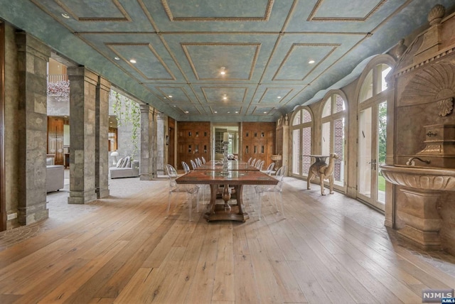 interior space with light hardwood / wood-style floors, ornate columns, and coffered ceiling