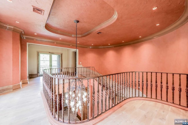 hall with hardwood / wood-style floors, ornamental molding, and a tray ceiling