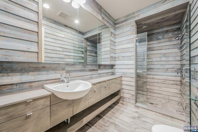 bathroom with hardwood / wood-style floors, wooden walls, sink, and a shower with shower door