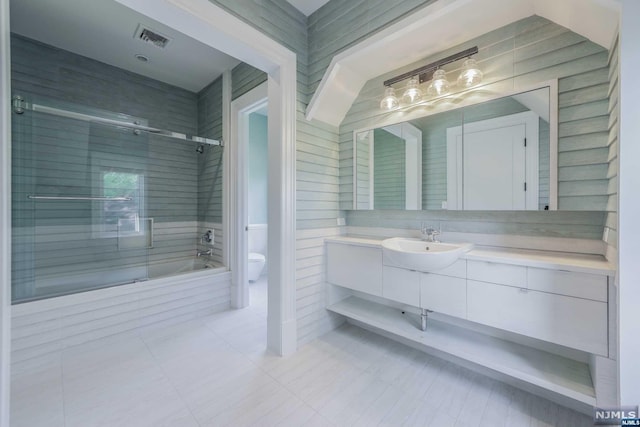 full bathroom with shower / bath combination with glass door, vanity, tile walls, and toilet