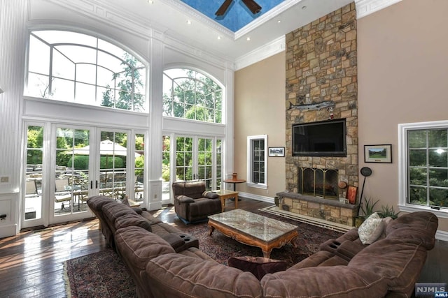 living room featuring wood-type flooring, a towering ceiling, a stone fireplace, and french doors