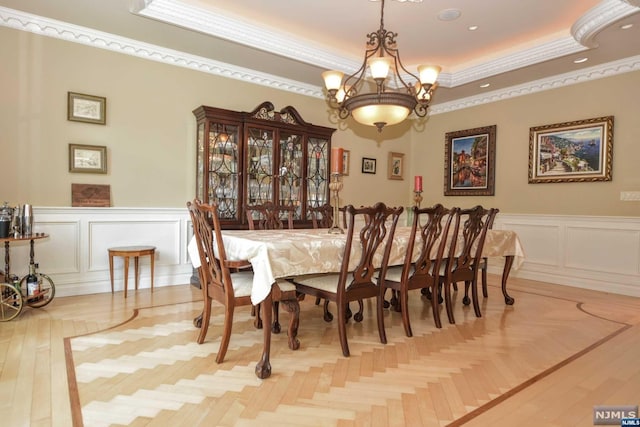 dining space with a notable chandelier, light wood-type flooring, crown molding, and a tray ceiling