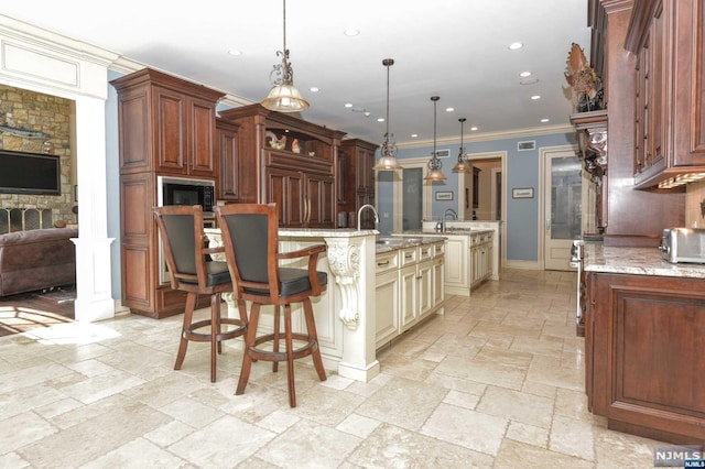 kitchen with pendant lighting, sink, light stone countertops, ornamental molding, and cream cabinetry