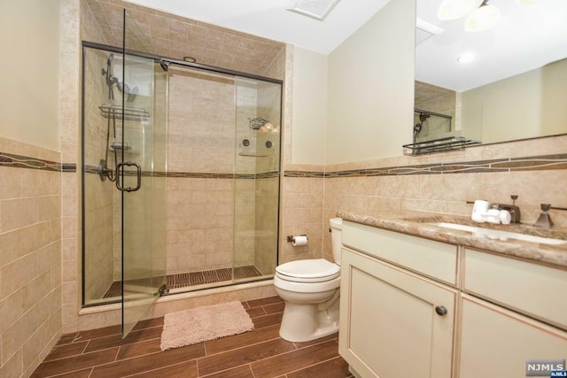 bathroom with vanity, toilet, a shower with door, and tile walls