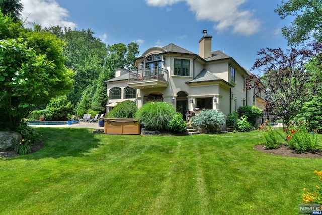 back of house with a lawn, a balcony, and a pool with hot tub