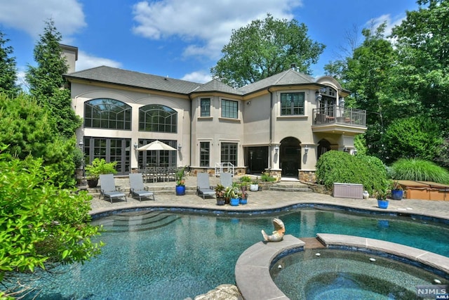 back of house with a swimming pool with hot tub, a balcony, and a patio