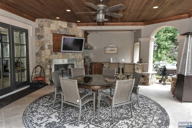 tiled dining area with french doors, an outdoor stone fireplace, ceiling fan, crown molding, and wooden ceiling