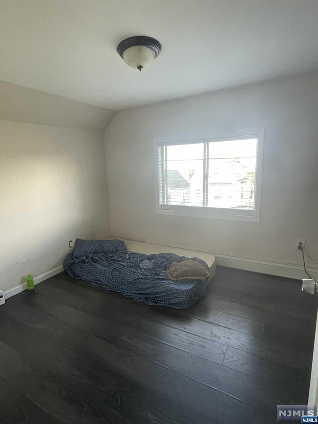 unfurnished bedroom featuring lofted ceiling and dark wood-type flooring