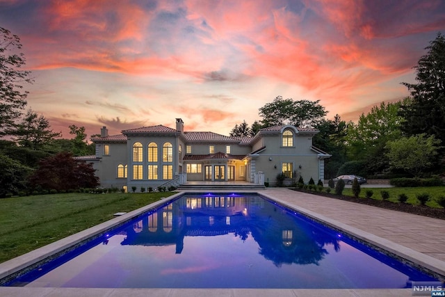 pool at dusk with a yard and a patio