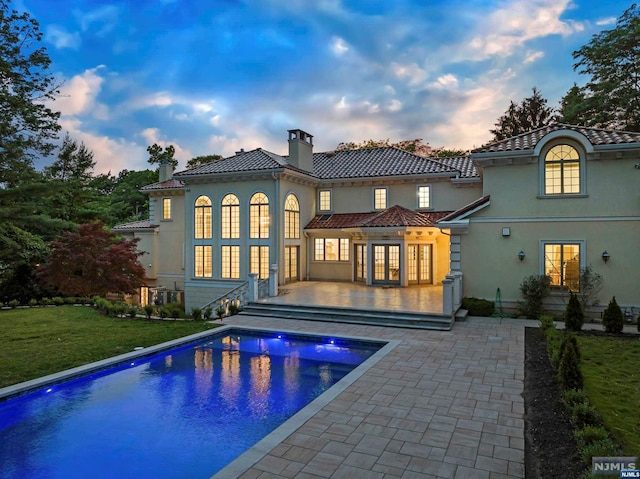 back house at dusk featuring a lawn, a patio, and french doors