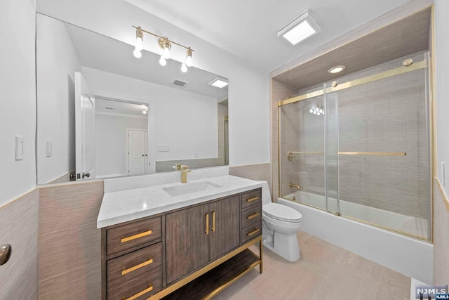 full bathroom featuring vanity, shower / bath combination with glass door, tile patterned flooring, toilet, and tile walls