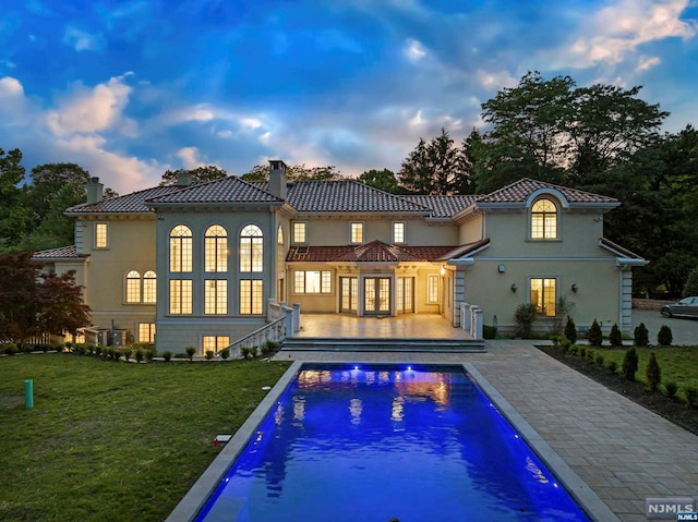 back house at dusk featuring a patio area and a yard