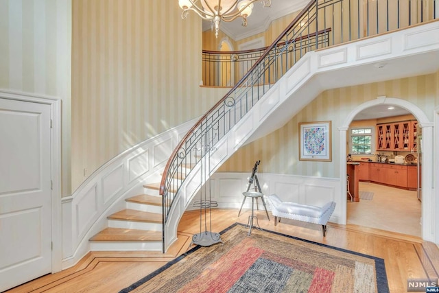 stairs with a chandelier, a high ceiling, crown molding, and wood-type flooring