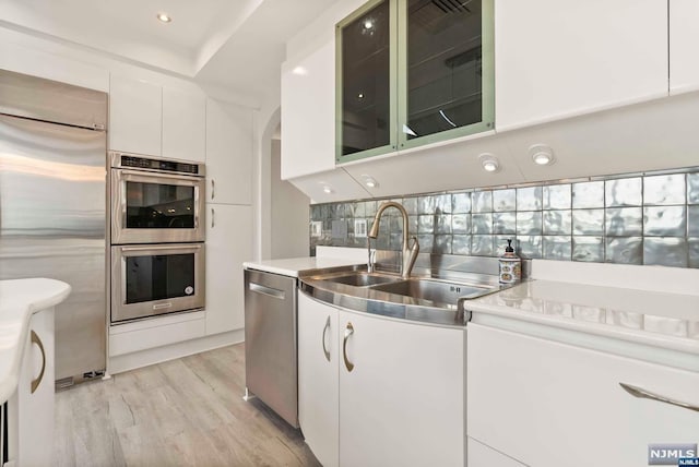 kitchen with tasteful backsplash, stainless steel appliances, sink, light hardwood / wood-style flooring, and white cabinets