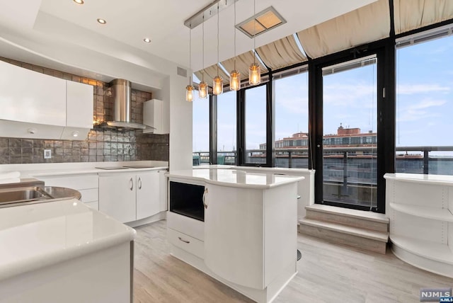 kitchen with backsplash, white cabinets, wall chimney exhaust hood, decorative light fixtures, and a kitchen island