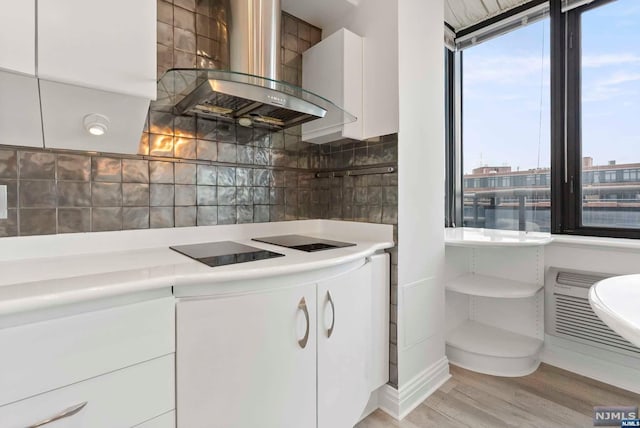 kitchen featuring wall chimney exhaust hood, tasteful backsplash, light hardwood / wood-style flooring, black electric stovetop, and white cabinets