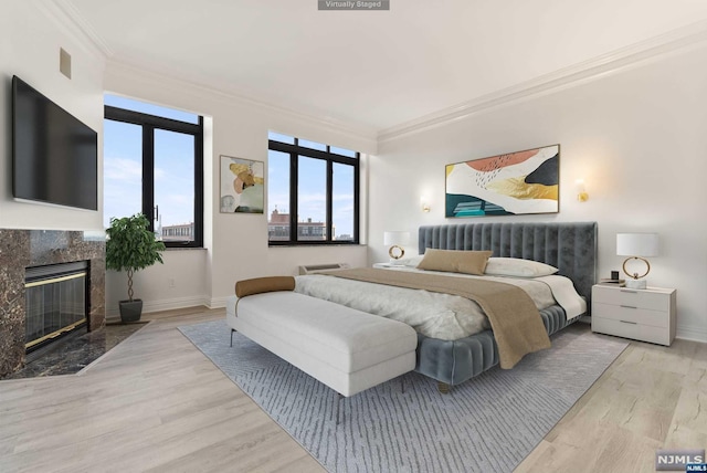 bedroom featuring crown molding, a high end fireplace, and light wood-type flooring