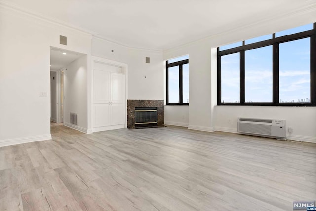 unfurnished living room with a premium fireplace, light wood-type flooring, ornamental molding, and a wall mounted AC