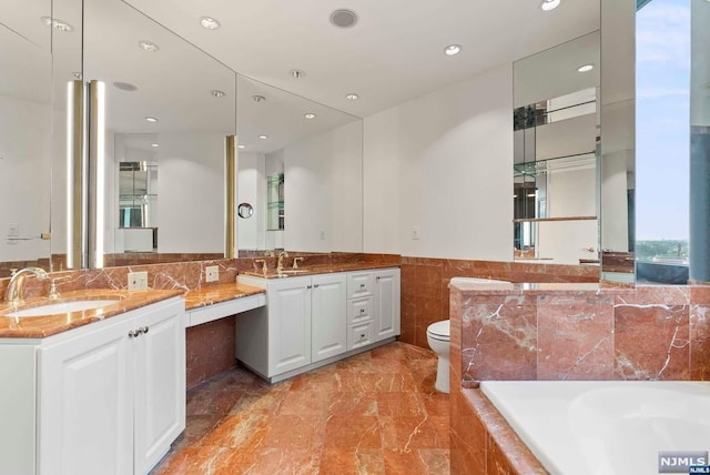 bathroom featuring vanity, a relaxing tiled tub, and toilet