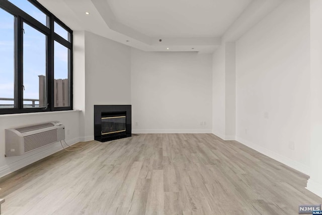 unfurnished living room with a wall mounted air conditioner and light hardwood / wood-style floors