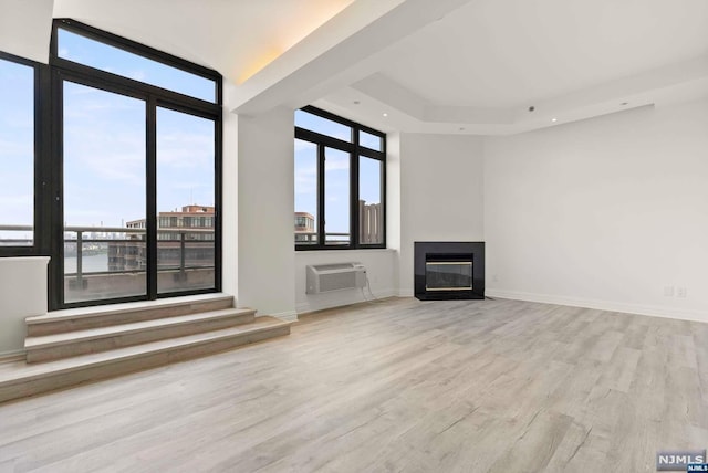 unfurnished living room with a wall mounted air conditioner, expansive windows, and light hardwood / wood-style flooring