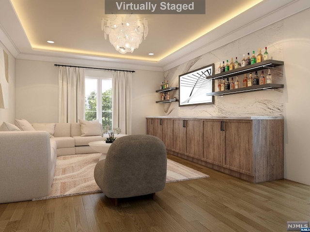 living area featuring hardwood / wood-style flooring, a raised ceiling, bar, and a notable chandelier