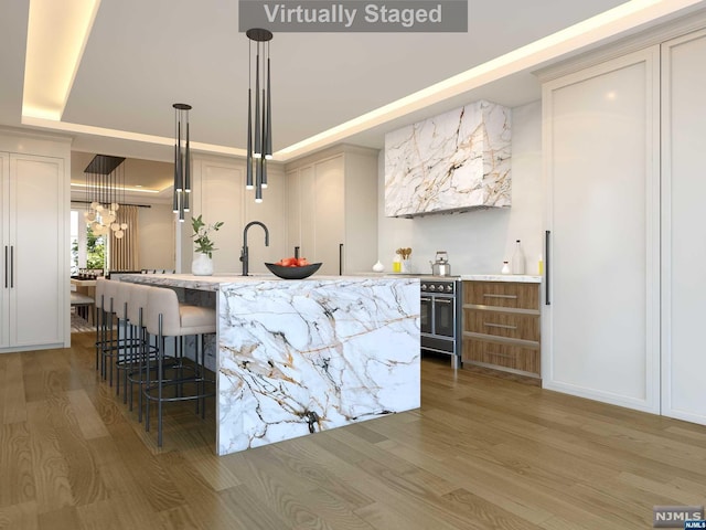 kitchen featuring pendant lighting, an inviting chandelier, an island with sink, light stone counters, and wood-type flooring