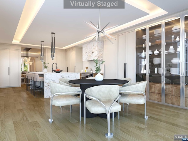 dining space with light wood-type flooring, an inviting chandelier, and a raised ceiling